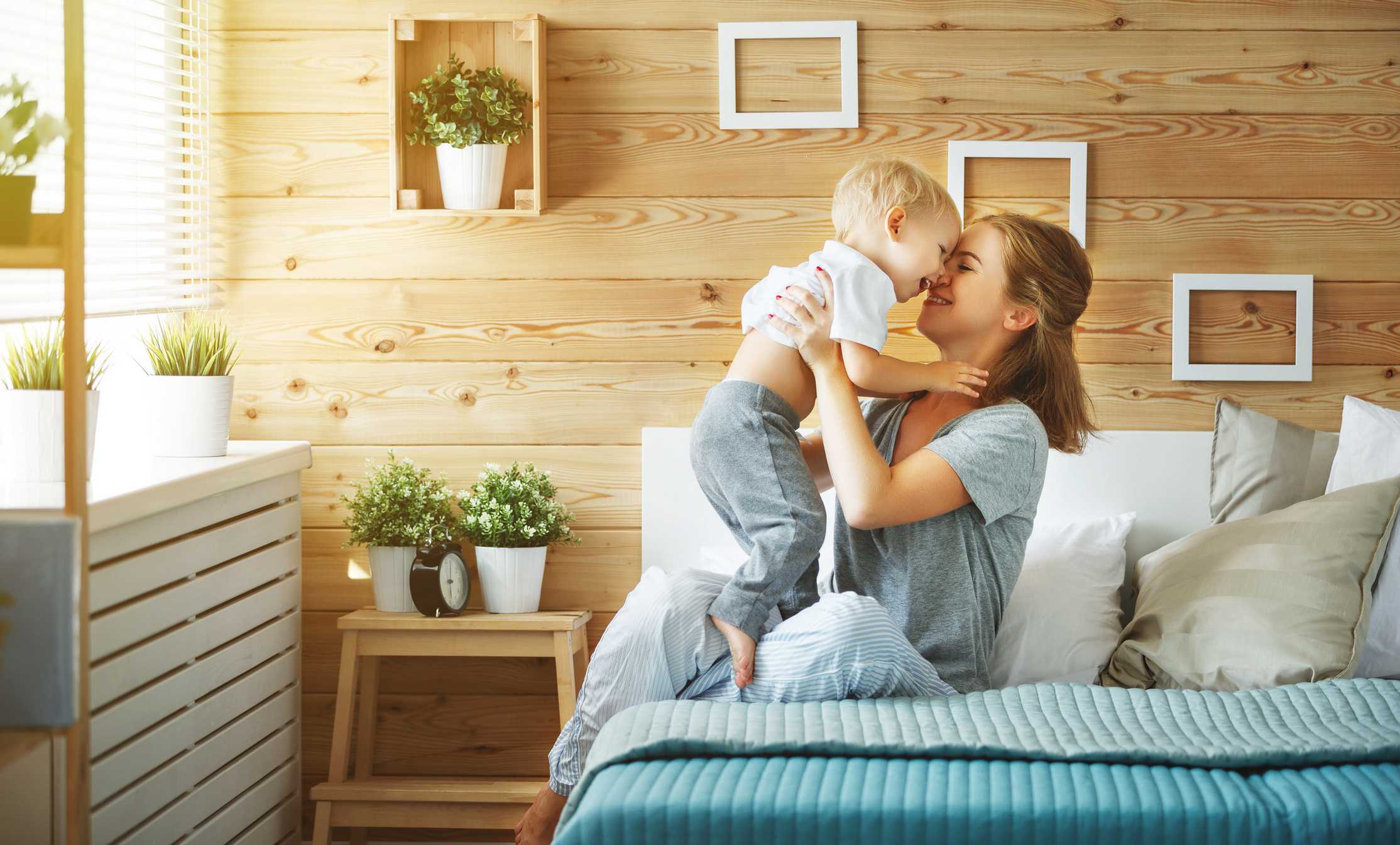 Mother and child sharing a joyful moment in a cozy, well-decorated bedroom with wooden walls and plants, emphasizing warmth and comfort in a home environment.