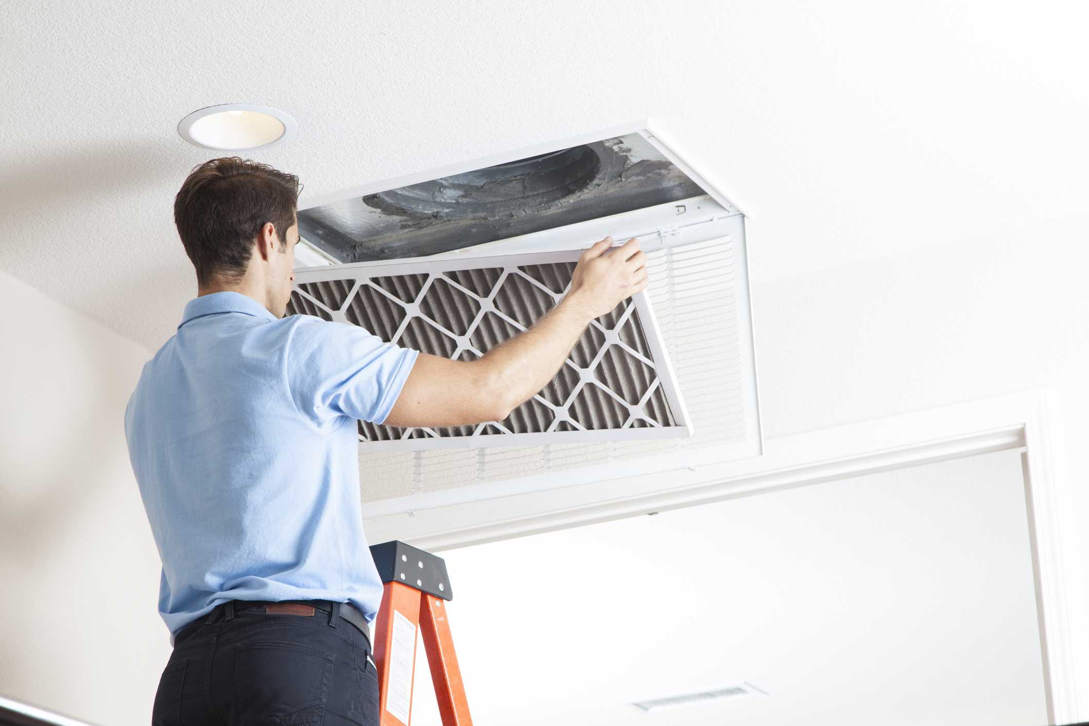 Man replacing an indoor air quality filter while standing on a ladder, emphasizing maintenance for improved home ventilation and air quality.