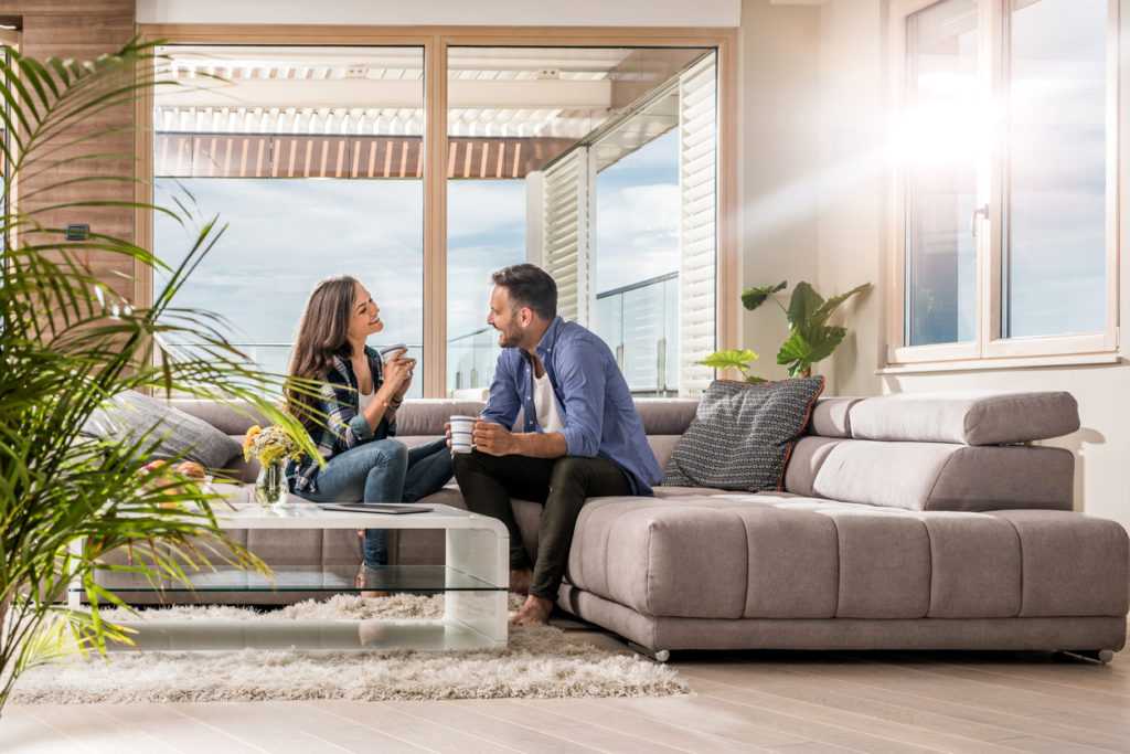 Couple enjoying conversation and drinks in a modern living room with natural light, emphasizing indoor comfort and air quality.