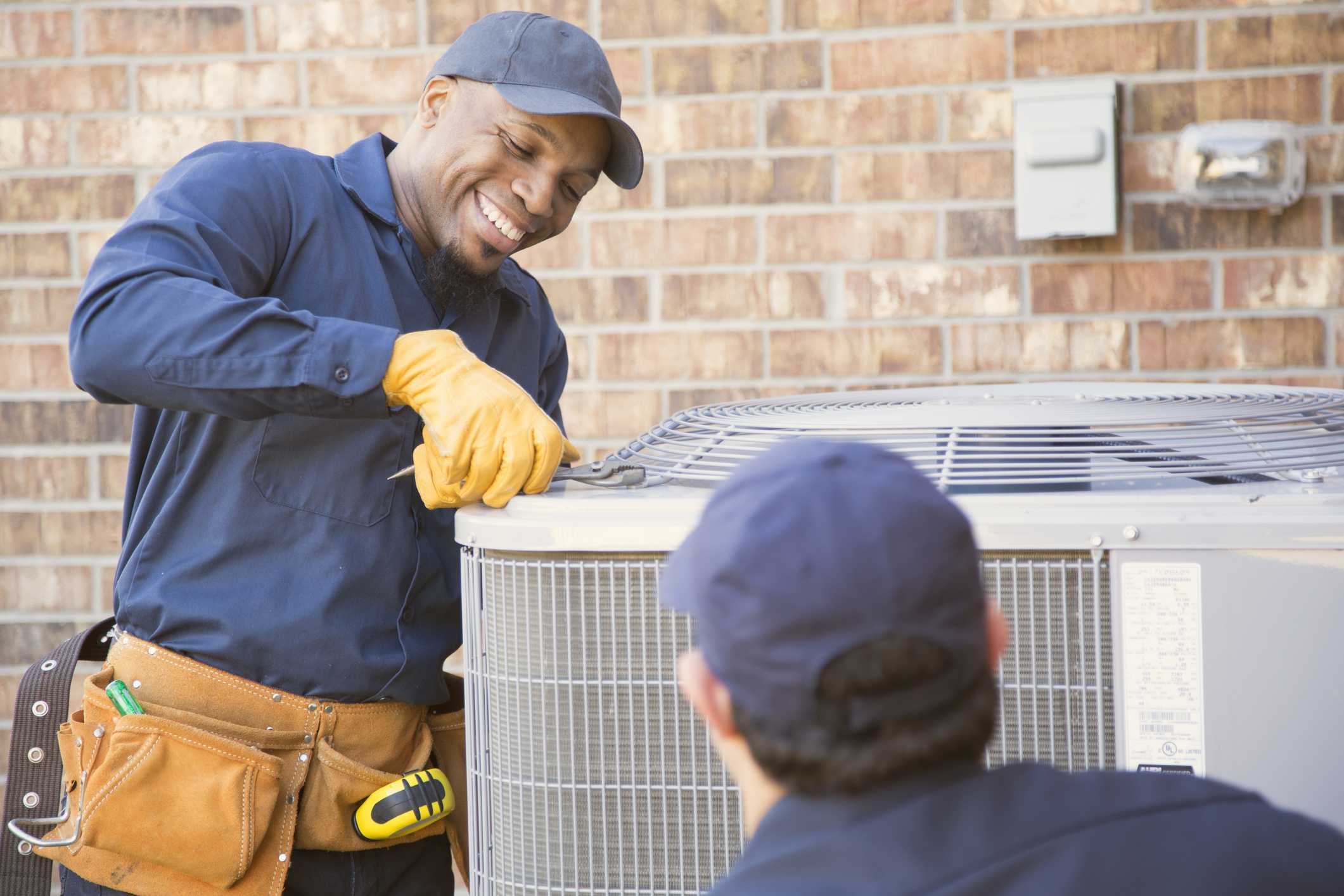 Technicians installing an air conditioning unit outdoors, smiling and collaborating, showcasing professional AC installation services in Phenix City, AL.